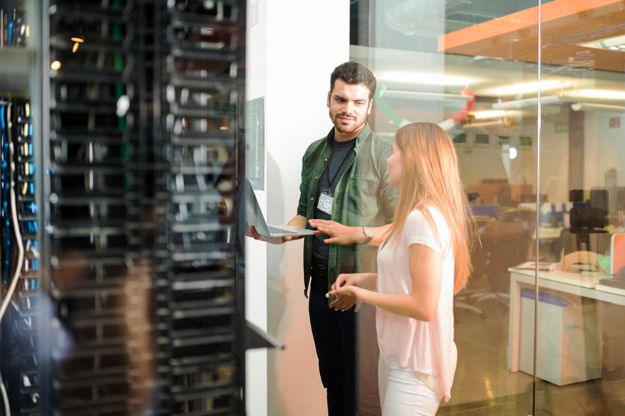 Two IT specialists reviewing a laptop in a server room